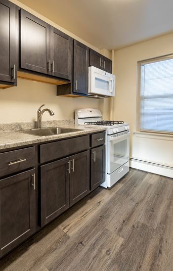 A kitchen with dark wood cabinets and a white stove top oven at Loch Bend Apartments, Baltimore, MD, 21234